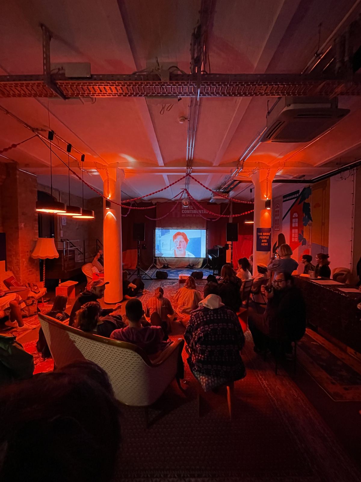 An early Movie Sprint screening in a small room lit red, an audience watching a projected film